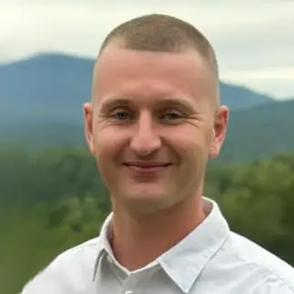 Smiling man in white shirt with blurred mountain landscape behind him